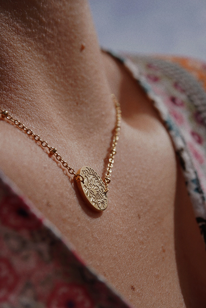 Collier doré avec une médaille aux motifs fleuris.