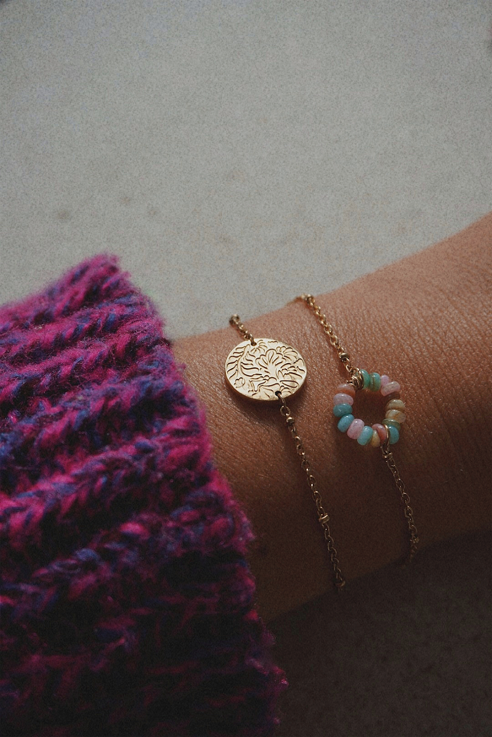 Bracelet doré avec une médaille aux motifs fleuris et bracelet avec des perles multicolores.