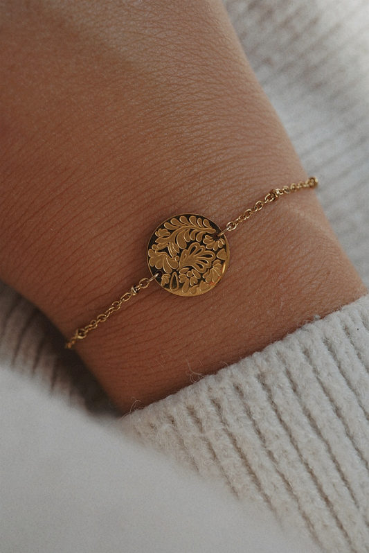 Bracelet doré avec une médaille aux motifs fleuris.