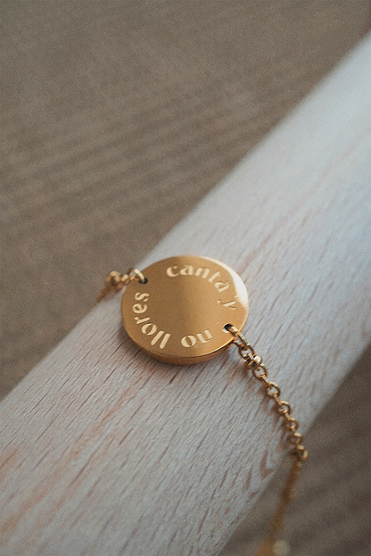Bracelet doré avec une médaille gravée avec une phrase.